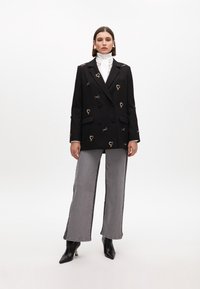 Černé dvouřadé sako s ozdobami ve tvaru srdce, v kombinaci se šedými širokými džínami a černými špičatými kotníkovými botami. Bílá halenka s vysokým límcem.