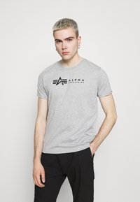 Grå kortermet T-skjorte laget av mykt stoff, med en svart "ALPHA INDUSTRIES" logo over brystet, supplert med en rund hals.