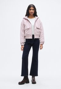 Ελαφρύ ροζ μπουφάν από κορντό, κοντό με κουκούλα, δύο μπροστινές τσέπες και ελαστικά μανίκια. Συνδυάζεται με σκούρα μπλε τζιν καμπάνα και καφέ μποτάκια μέχρι τον αστράγαλο.