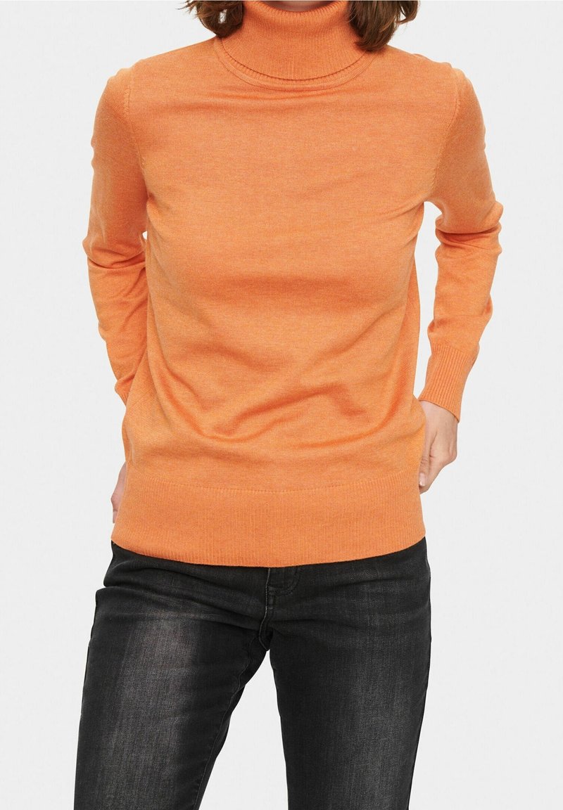 Orange turtleneck-tröja i mjukt stickat material, med långa ärmar och en figurnära design. Kombinerad med mörka jeans.