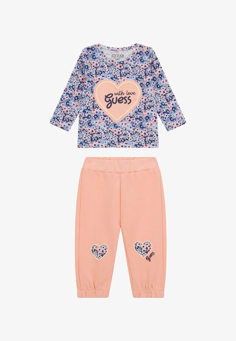 Maglietta a maniche lunghe con un motivo floreale blu e rosa, caratterizzata da una grafica a forma di cuore; pantaloni rosa abbinati con toppe a forma di cuore e polsini arricciati.