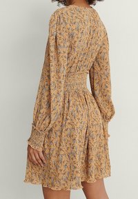 Vestido amarillo de flores de manga larga con cintura fruncida y dobladillo con volantes. Presenta una textura suave y una tela ligera.