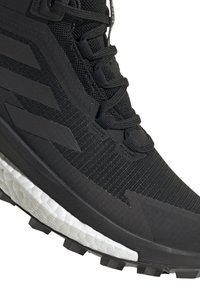 Black athletic shoe featuring a textured upper, contrasting rubber sole, and notable traction spikes. Sleek design with lacing system.