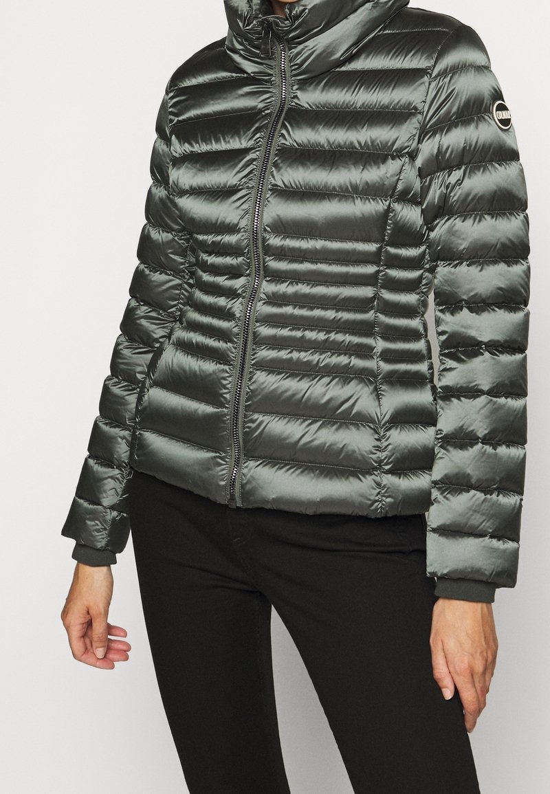 Polstrad grön puffjacka med hög krage, dragkedja fram och ribbade ärmar. Utmärkande horisontell sömnad och glänsande textur.