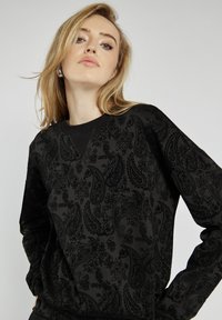 Czarna bluza z tonalnym wzorem paisley, okrągłym dekoltem i długimi rękawami, o miękkiej fakturze i luźnym kroju.