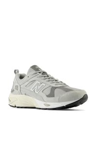 Graue Sport Schuhe aus einer Kombination von Wildleder und Mesh-Material, mit einem weißen N-Logo, dicker Sohle und strukturierten Akzenten.