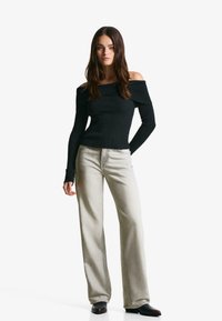 Svart ribbad off-shoulder topp med långa ärmar, ihop med ljusgrå vida jeans. Jeansen har synlig sömnad och fickor.