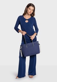 Sac à main bleu marine avec deux anses, en tissu. Présente une forme rectangulaire, une texture lisse et des accents contrastants en bleu marine et crème.
