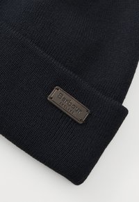 Gorro de malha azul-marinho com textura canelada e um pequeno rótulo em metal marrom gravado com "Barbour England."