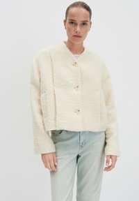 Gekruide crèmekleurige textuurjacket met een ronde halslijn, vier knopen en lange mouwen, gecombineerd met lichtblauwe spijkerbroek.