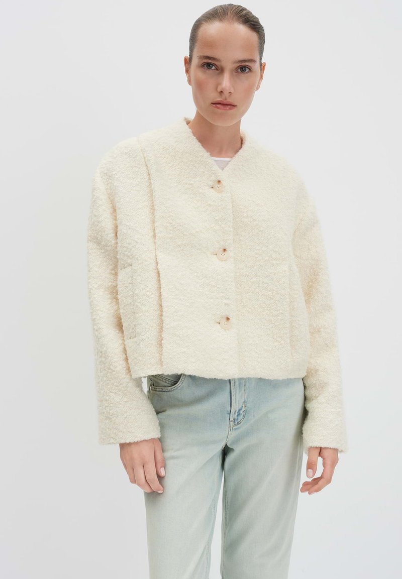 Gekruide crèmekleurige textuurjacket met een ronde halslijn, vier knopen en lange mouwen, gecombineerd met lichtblauwe spijkerbroek.