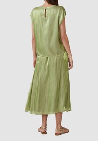 Langes, fließendes Kleid aus leichtem, grünem Satin mit einem Schlüsselaugen-Detail am Rücken. Es hat kurze Ärmel und eine lockere Passform für mehr Beweglichkeit und Komfort.