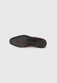 Zapato de cuero marrón con una suela curva de goma negra. Presenta un acabado suave, un agarre texturizado en la parte inferior y un diseño elegante.