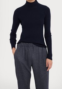 Maglione a collo alto navy a costine con maniche lunghe, abbinato a pantaloni scuri grigi a fantasia con fascia elastica in vita e un delicato motivo a spina di pesce.