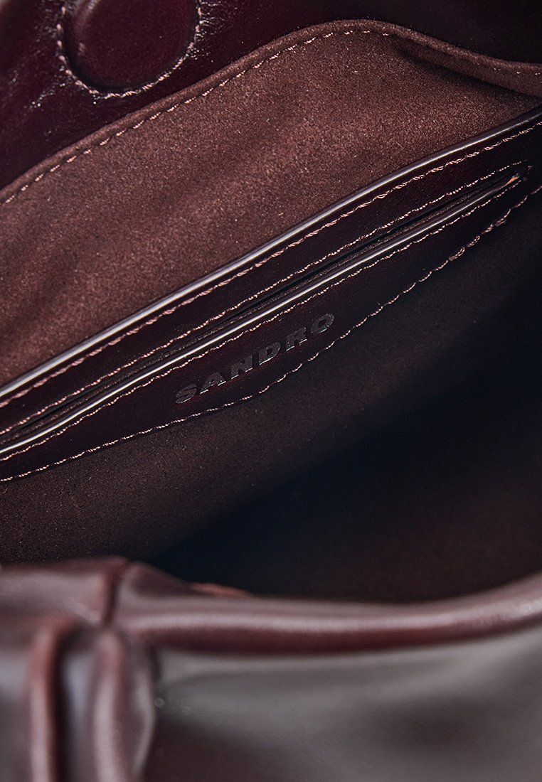 Intérieur d'un sac en cuir bourgogne à texture douce, avec une poche zippée et une étiquette en relief "SANDRO". Des coutures douces mettent en valeur le design.