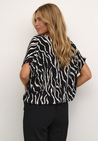 Černobílé tričko se zebra pruhy, krátkými rukávy, lehkým materiálem, volným střihem a kulatým výstřihem. Kombinováno s černými kalhotami.