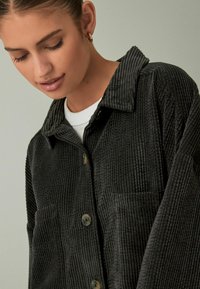 Zwart corduroy overhemdjacket met een gestructureerd oppervlak, voorzien van een kraag, een knoopsluiting aan de voorkant en twee zakken.