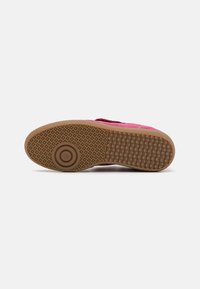 Chaussure en daim rose avec une semelle en caoutchouc texturé, comportant un accent circulaire et un motif de petites rainures pour l'adhérence.