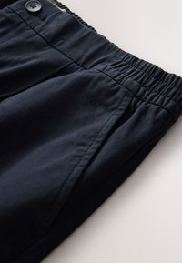 Donkerblauwe broek met een elastische tailleband, voorzien van een knoopsluiting en zijzakken. Gemaakt van gladde, lichte stof.