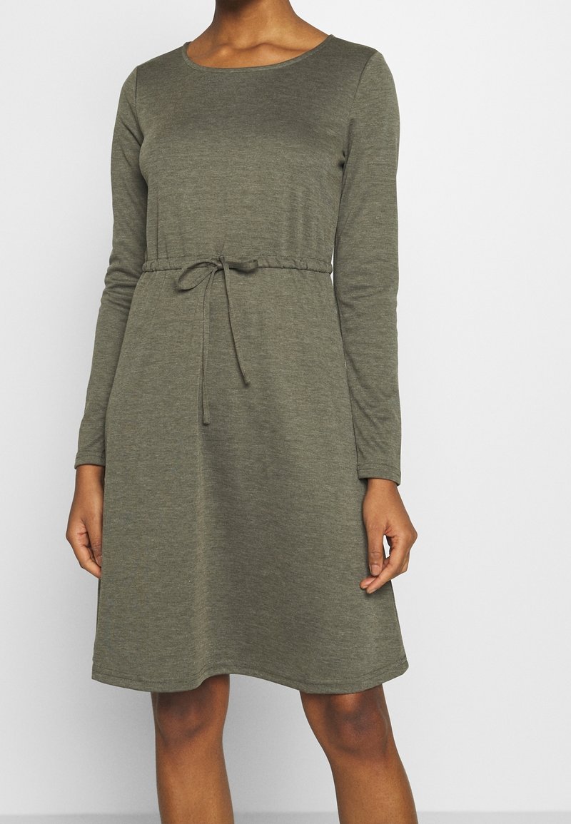 Zielono-oliwkowa sukienka z długim rękawem, okrągłym dekoltem i paskiem na sznurek w talii. Wykonana z miękkiej, teksturowanej tkaniny o luźnym kroju.