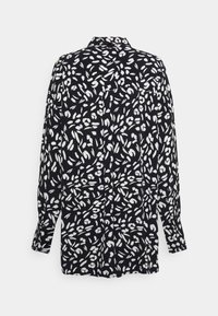 Langarmshirt met een zwarte achtergrond en een wit abstract patroon, featuring een kraag en knoopsluiting achter.