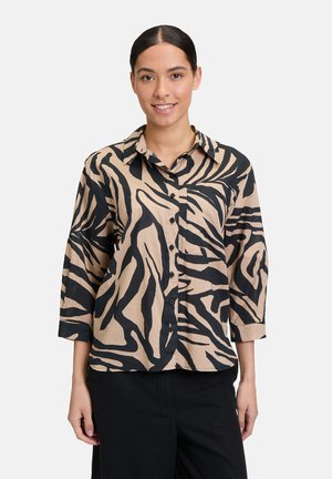 Beige Hemd mit Knopfleiste und einem schwarzen Zebra-Streifenmuster, mit Kragen und Dreiviertelärmeln. Glatte Stofftextur.