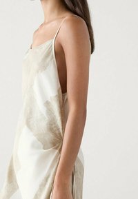 Robe sans manches de couleur crème avec des motifs abstraits beiges. Fabriquée en tissu léger, elle présente une coupe décontractée et des bretelles délicates.