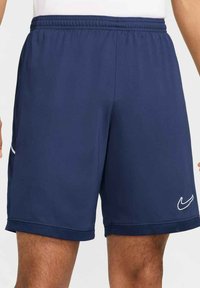 Navyblaue Sportshorts mit elastischem Bund, seitlichen Taschen und weißem Nike-Logo. Hergestellt aus leichtem, atmungsaktivem Stoff mit glatter Textur.