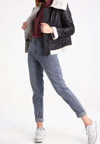 Svart läderjacka i fårskinn med en kort design och sidobanddetalj, kombinerad med ljusblå jeans med uppvikt kant och vita sneakers.