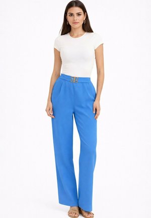 Femme portant un haut blanc ajusté à manches courtes, un pantalon large bleu vif taille haute avec une ceinture décorative et des sandales beige.