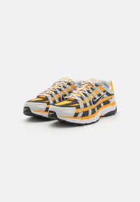 Tenisky Nike s vrškem ze síťoviny a syntetického materiálu v šedé, černé a oranžové barvě. Mají polstrovanou podrážku, bílé šňůrky a texturované akcenty.