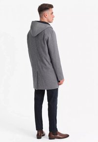 Abrigo de cuadro de galgo gris con capucha, que presenta un corte recto y botones ocultos, combinado con pantalones oscuros y botas de tobillo marrones.