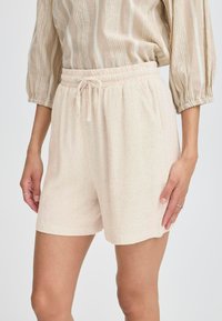 Pantaloni corti beige chiaro realizzati in un tessuto strutturato, con vita elasticizzata e cordoncino, e tasche laterali.