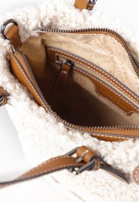 Tan leren accenten benadrukken deze crèmekleurige textuur van de bucket bag. Het heeft een ritssluiting en een binnenvak met een gestreepte voering.