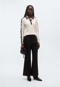 Ljus krämfärgad långärmad pikétröja med svarta leopardmönstrade detaljer, kombinerad med svart, höga vida byxor och svart handväska.