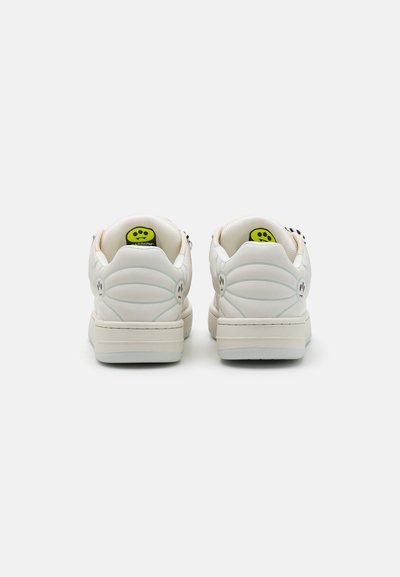 Sneakers bianchi in pelle texturizzata, con un design a profilo basso e un logo verde sul tallone. Presentano forme morbide e arrotondate con dettagli di cucitura.