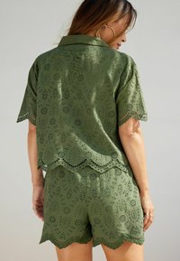 Olive roheline kaheosaline komplekt, millel on tikandiga ülaosa, lainelise äärise ja lühikeste varrukatega, koos vastava lühikeste pükstega.