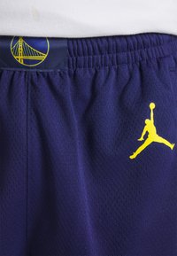 Shorts de sport bleu foncé avec logo jaune des Golden State Warriors à la taille et logo jaune Jumpman sur la cuisse.