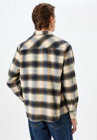 Ruteret flannel skjorte i gul, grå og marineblå. Har en spids krave, knapmanchetter og en lige kant med sideslidser.