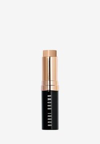 Rouge à lèvres dans un étui cylindrique noir avec un capuchon métallique doré. Présente un dessus carré et le texte "BOBBI BROWN" sur le côté en blanc.