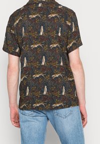 Camicetta a maniche corte in tessuto scuro, con un motivo animale multicolore e accenti beige e verdi. Vestibilità casual con colletto.