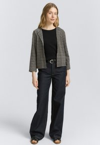 Blazer rayé noir et blanc avec des manches trois-quarts, associé à un haut noir et un pantalon large en denim sombre taille haute.