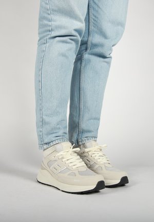 Lichtgrijze sneakers met een getextureerde mesh bovenzijde, vetersluiting aan de voorkant en een zwarte rubberen zool, gecombineerd met lichtblauwe opgerolde spijkerbroek.