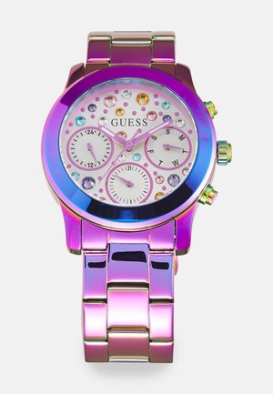 Bunt gefärbte Guess-Uhr mit einem glänzenden, schillernden violetten Metallarmband, Edelsteinelementen auf dem Zifferblatt und drei Teilzeigern zur Zeitmessung.