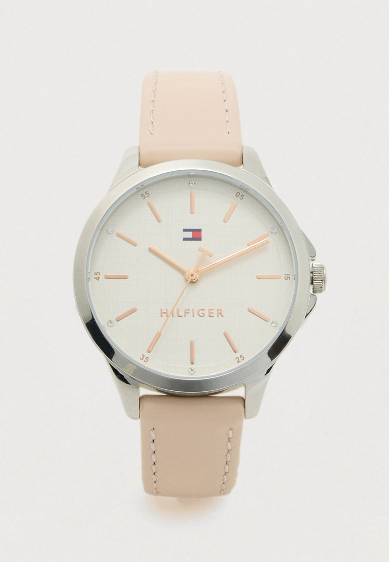 Pyöreä hopeanvärinen rannekello, jossa on beige nahkahihna, vaalea kellotaulu, ruusukultaiset tuntimerkit ja viisarit sekä pieni punainen, valkoinen ja sininen logo kello 12:n kohdalla.