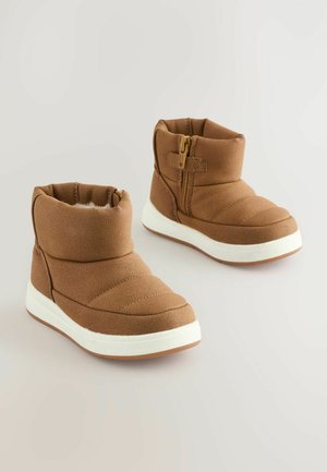 Barna steppelt csizmák puha textúrával, oldalsó cipzárral és fehér gumitalppal. Lekerekített dizájn, párnázott boka védelmmel.