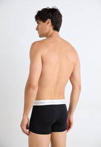Zwarte katoenen boxershorts met een witte tailleband waarop het "Calvin Klein" logo staat, gezien van achteren, met een accent op het aansluitende ontwerp.