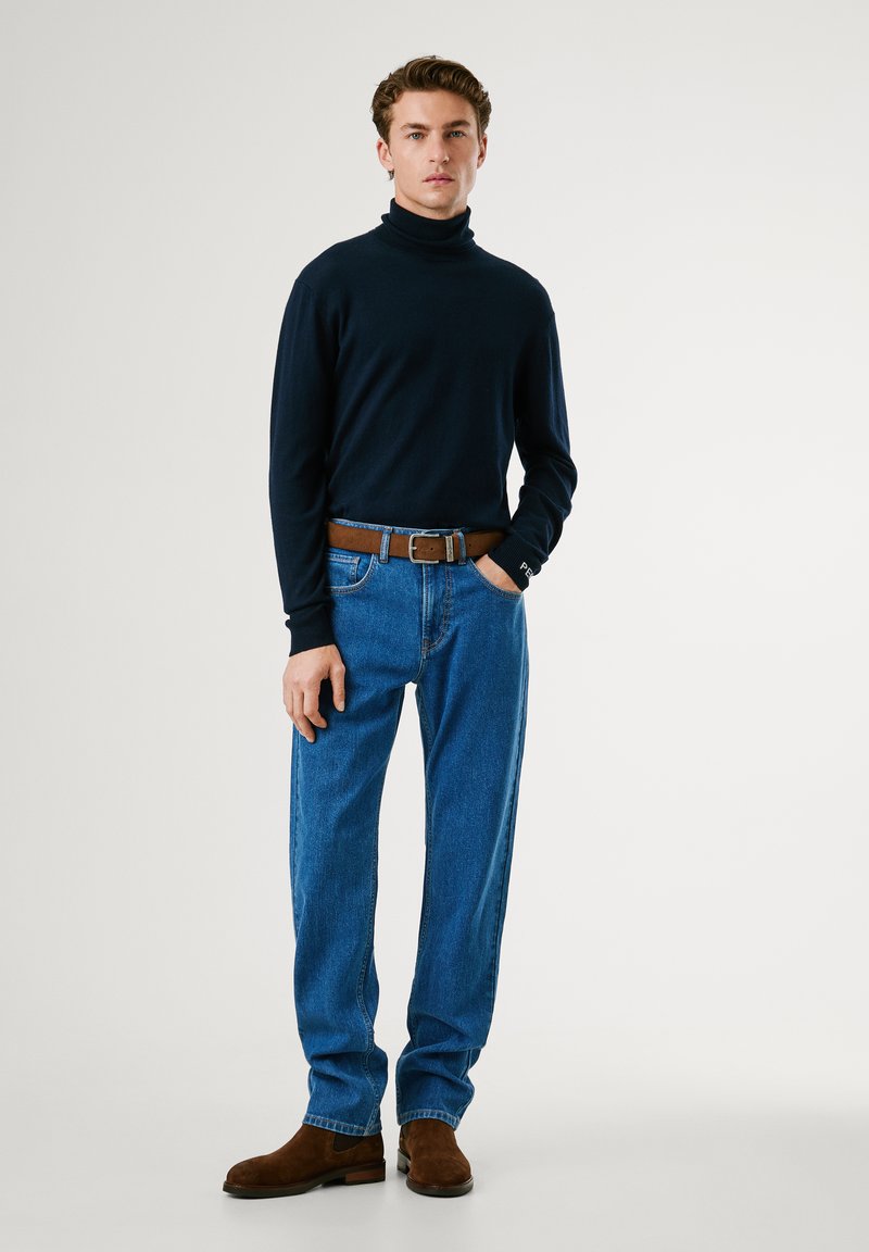 Granatowy sweter z golfem połączony z niebieskimi jeansami. Brązowy skórzany pasek i brązowe zamszowe botki za kostkę dopełniają stylizację. Prosty design, casualowy krój.