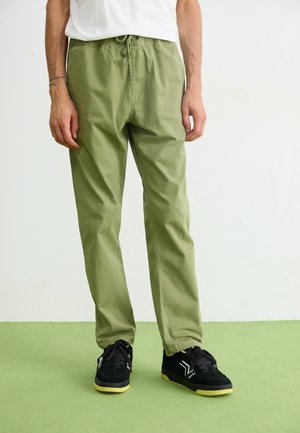 Olive green drawstring pants made of a lightweight fabric with a relaxed fit, paired with black sneakers featuring yellow accents.