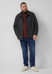 Szara kurtka z mieszanki wełny z zapięciem na guziki, kieszenią na piersi, noszona na bordowym golfie, zestawiona z niebieskimi dżinsami i jasnymi sportowymi butami.